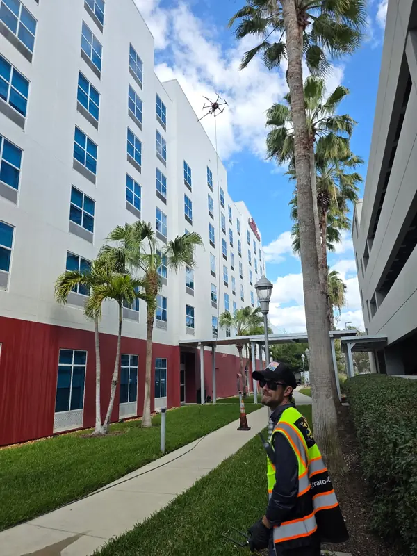 Operator in a hi-vis vest controlling the cleaning drone from the ground beside the hotel